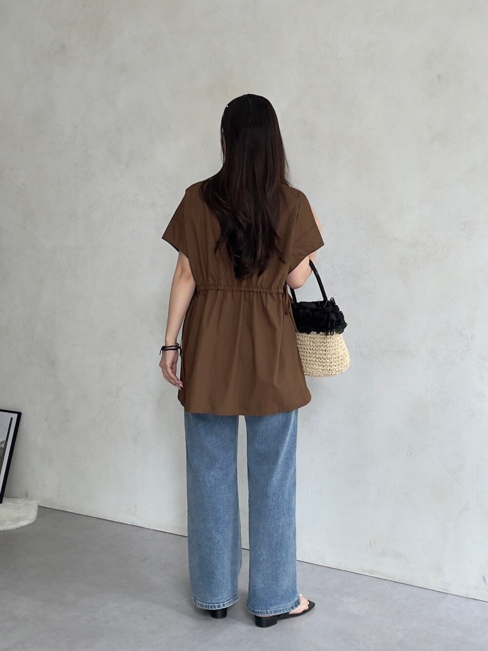 ベージュ系のかごバッグ、ブルー系のデニムパンツ、ブラック系のサンダルを着用したレディースの夏コーディネートの3枚目の写真