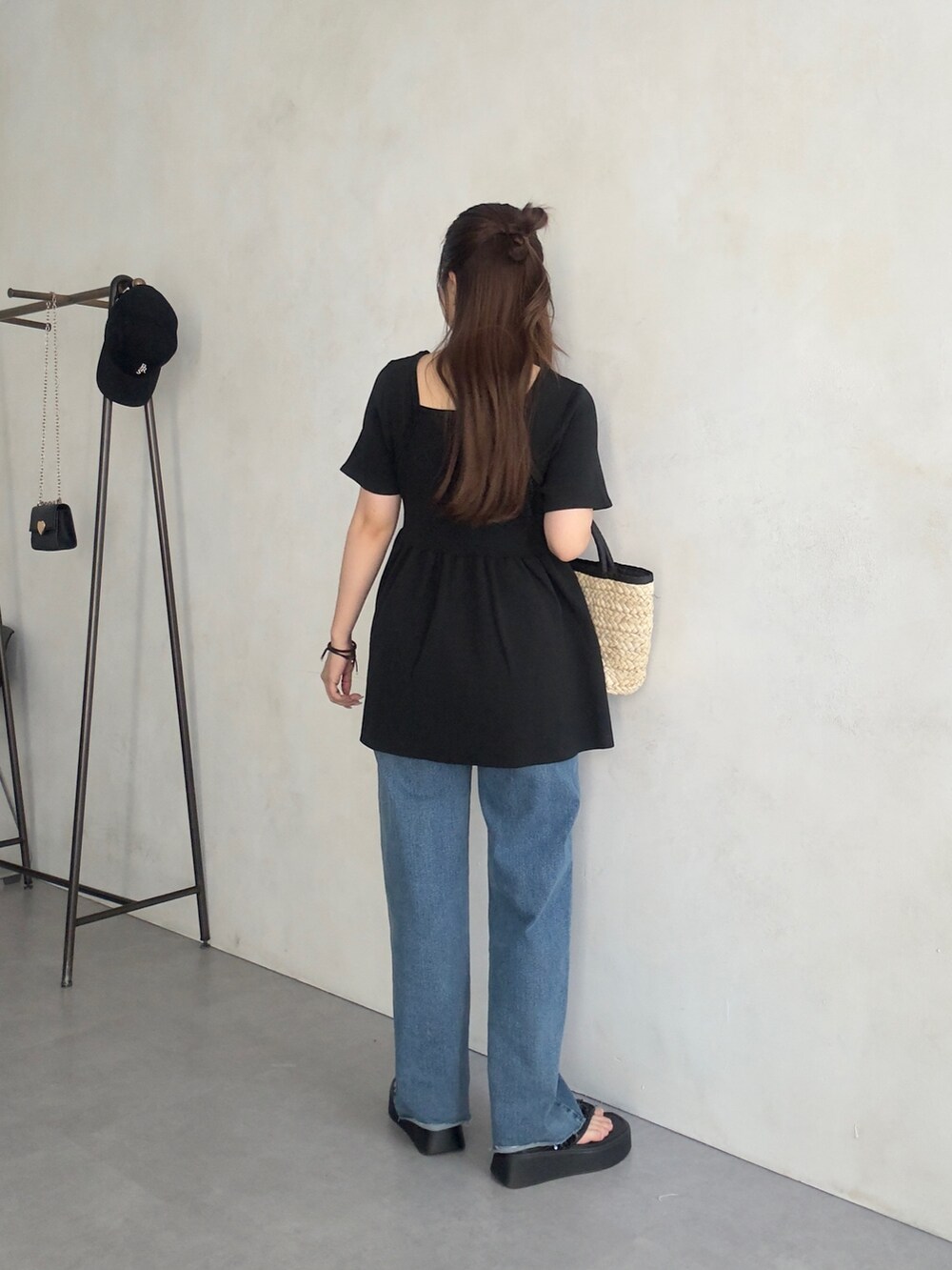 ブラック系のニット/セーター、ブラック系のかごバッグ、ブルー系のデニムパンツを着用したレディースの夏コーディネートの3枚目の写真