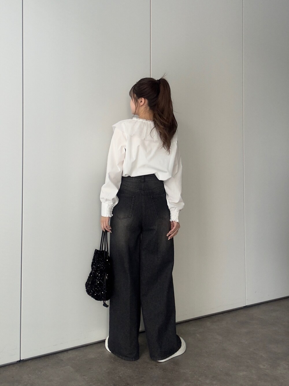 ブラック系のデニムパンツ、ホワイト系のスニーカー、ブラック系のショルダーバッグを着用したレディースの冬コーディネートの3枚目の写真