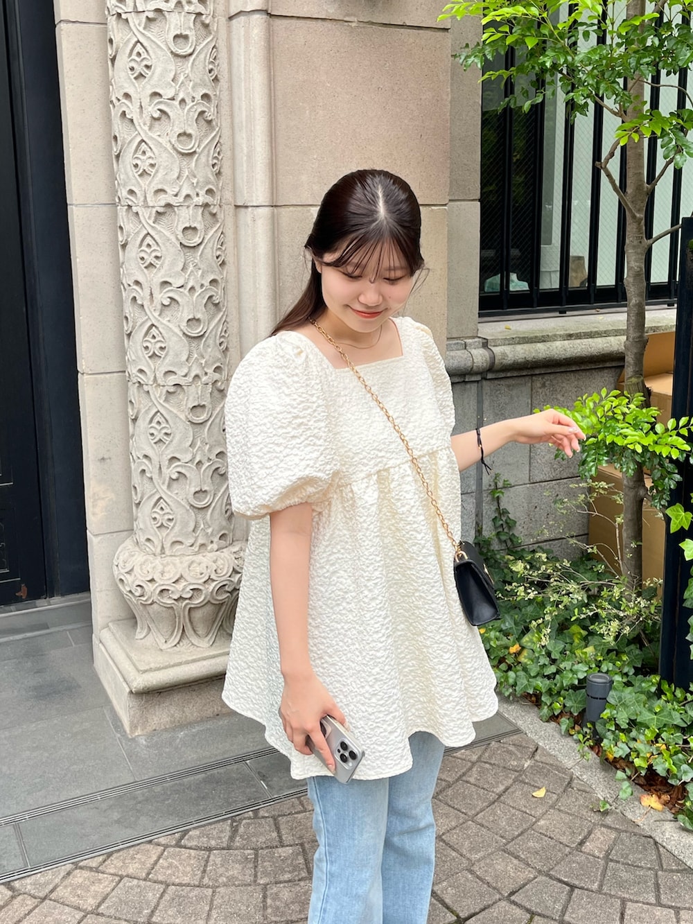ブラック系のショルダーバッグ、ブルー系のデニムパンツ、ブラック系のパンプスを着用したレディースの春コーディネートの2枚目の写真