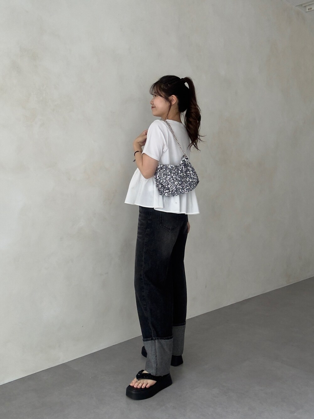 シルバー系のショルダーバッグ、ブラック系のデニムパンツ、ブラック系のサンダルを着用したレディースの夏コーディネートの2枚目の写真