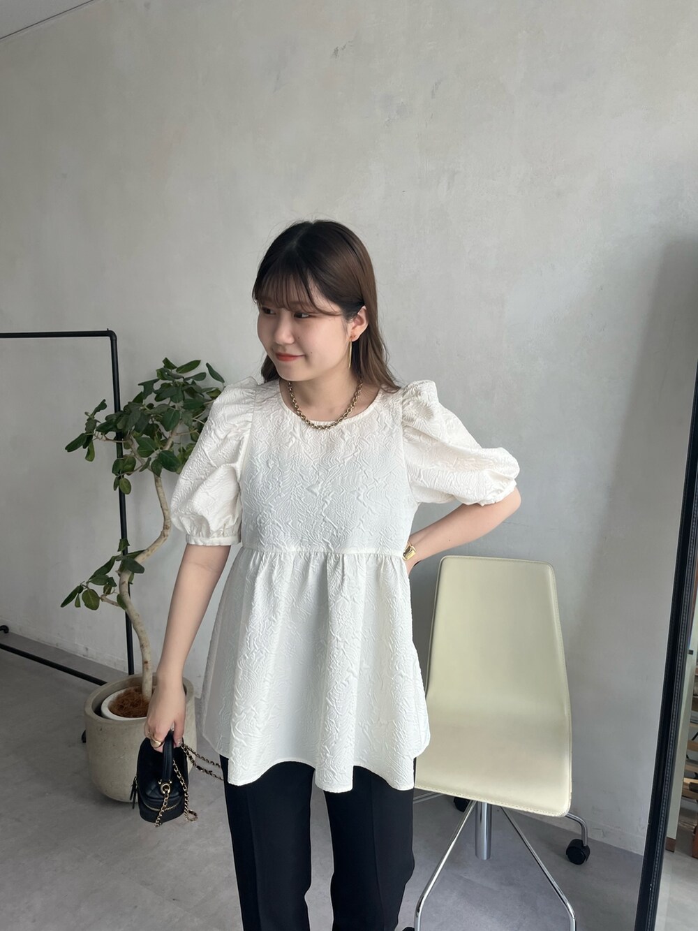 ブラック系のショルダーバッグ、ホワイト系のパンツドレス、ゴールド系のネックレスを着用したレディースの春コーディネートの2枚目の写真