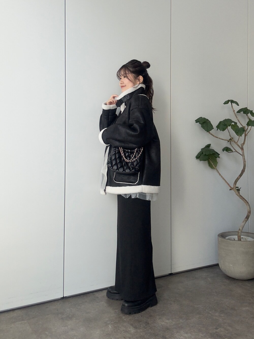 ブラック系のムートンコート、ブラック系のショルダーバッグ、ホワイト系のニット/セーターを着用したレディースの冬コーディネートの2枚目の写真