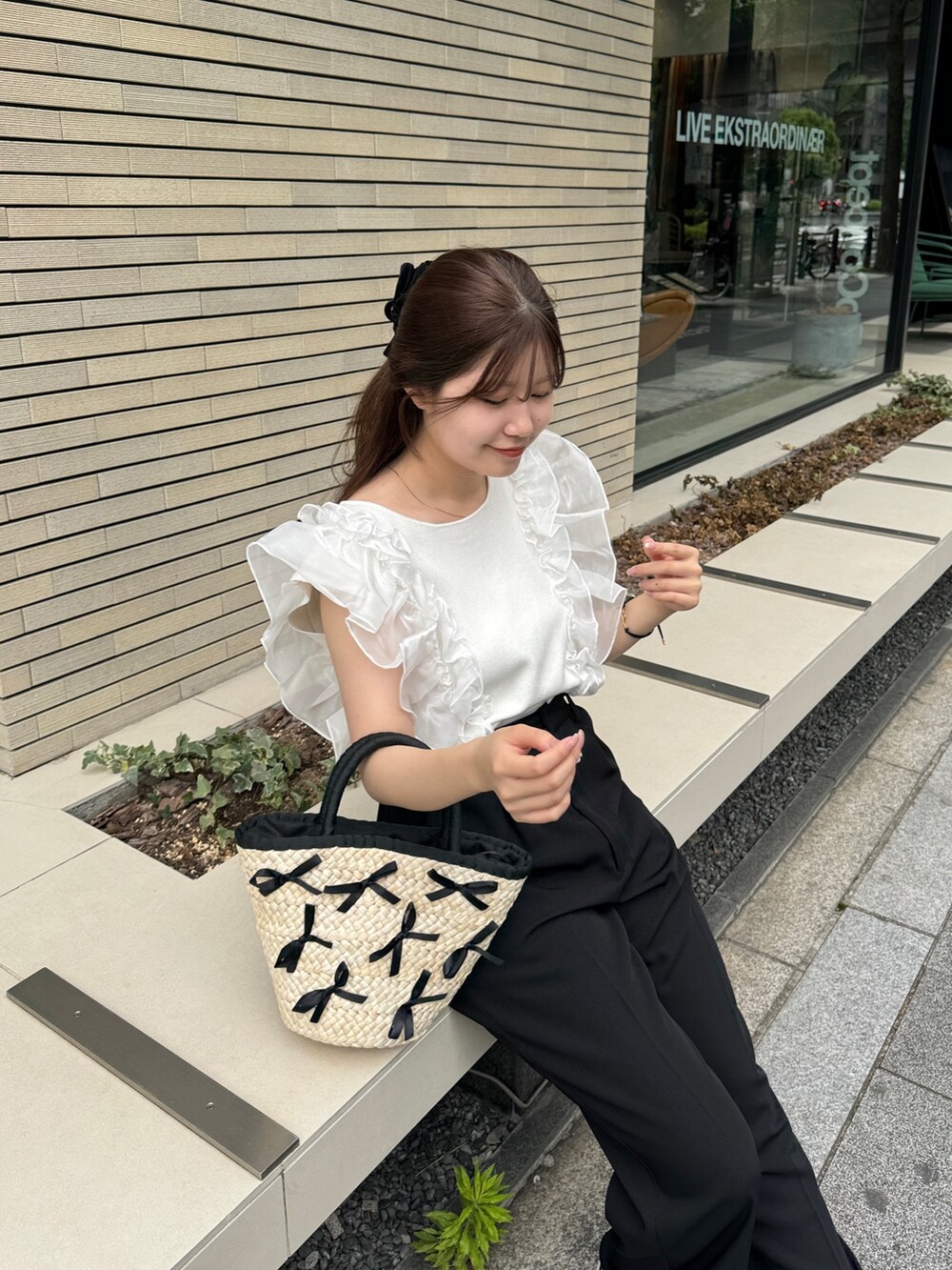 ブラック系のスラックス、ブラック系のかごバッグ、ホワイト系のニット/セーターを着用したレディースの夏コーディネートの2枚目の写真