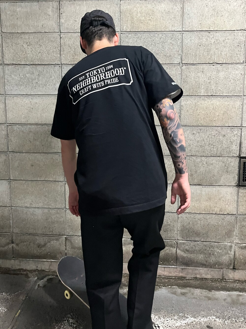 ブラック系のTシャツ/カットソー、ブラック系のチノパンツ、ホワイト系のスニーカーを着用したメンズの夏コーディネートの2枚目の写真