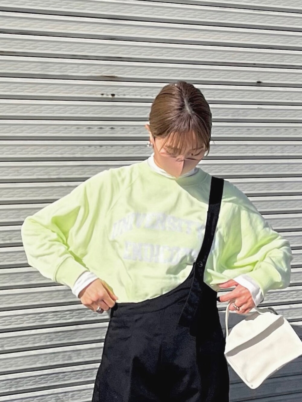 イエロー系のスウェット、グレー系のスニーカー、ブラック系のサロペット/オーバーオールを着用したレディースの冬コーディネートの2枚目の写真