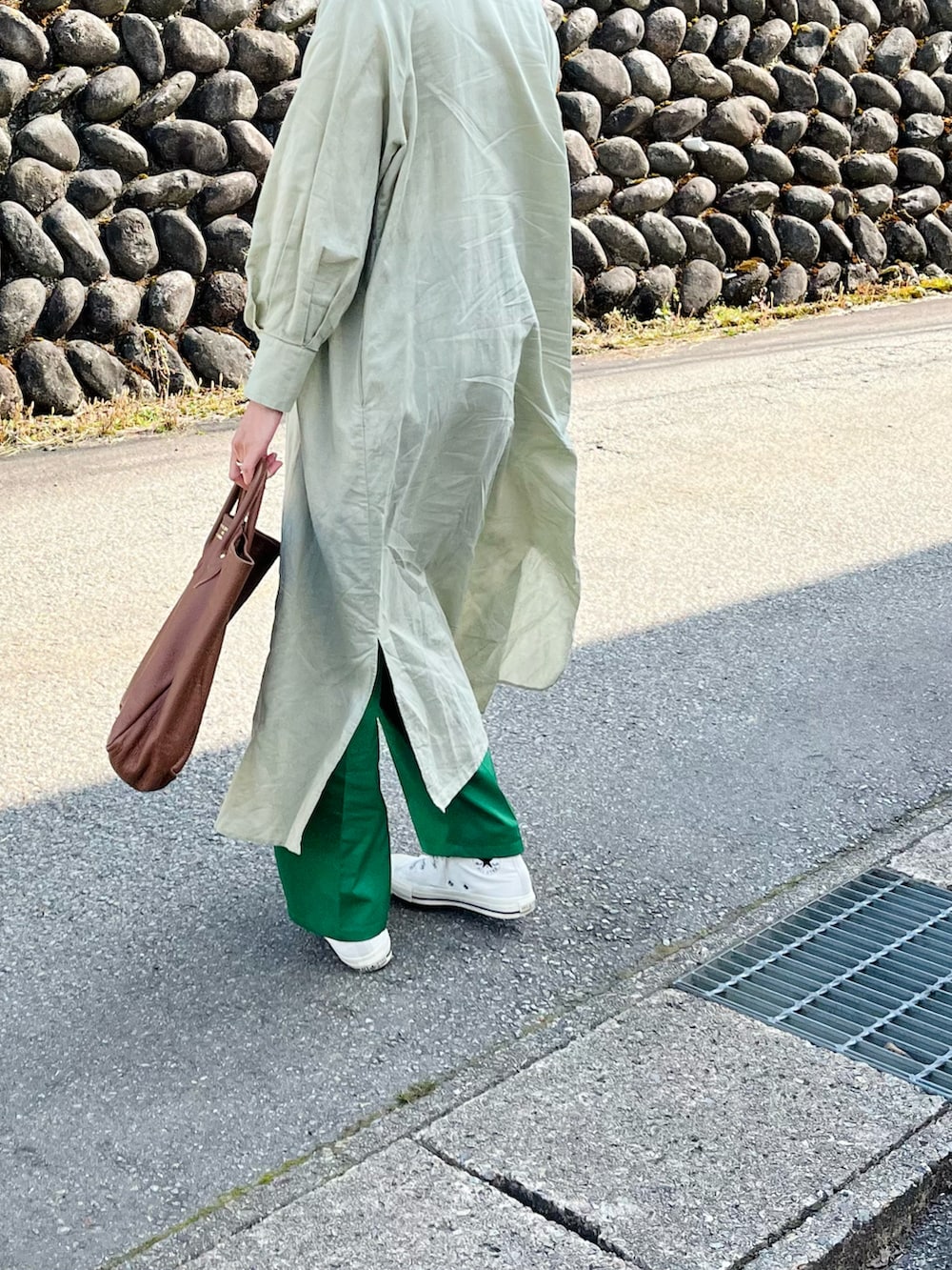 グリーン系のスラックス、ブラウン系のトートバッグ、ホワイト系のスニーカーを着用したレディースの春コーディネートの2枚目の写真