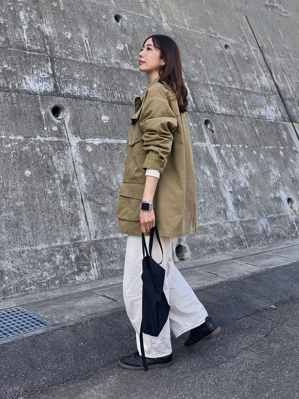 イエロー系のミリタリージャケット、ブラック系のショルダーバッグ、ホワイト系のデニムパンツを着用したレディースの春コーディネートの2枚目の写真