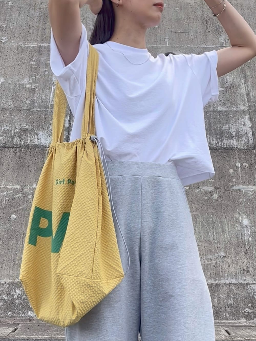 イエロー系のトートバッグ、グレー系のパンツ、ブラック系のスニーカーを着用したレディースの夏コーディネートの4枚目の写真