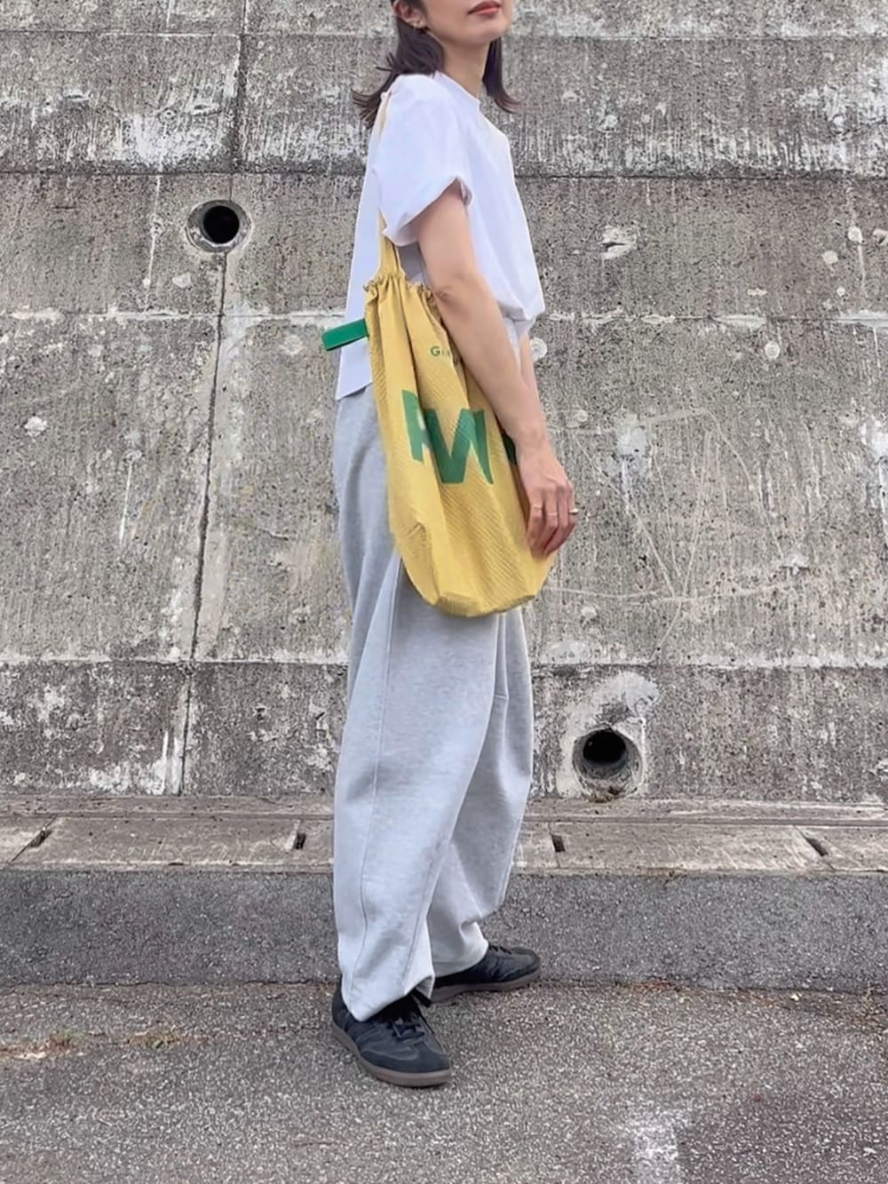 イエロー系のトートバッグ、グレー系のパンツ、ブラック系のスニーカーを着用したレディースの夏コーディネートの3枚目の写真
