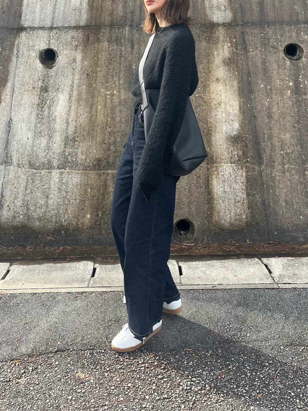 ブルー系のデニムパンツ、ブラック系のニット/セーター、ブラック系のショルダーバッグを着用したレディースの冬コーディネートの2枚目の写真