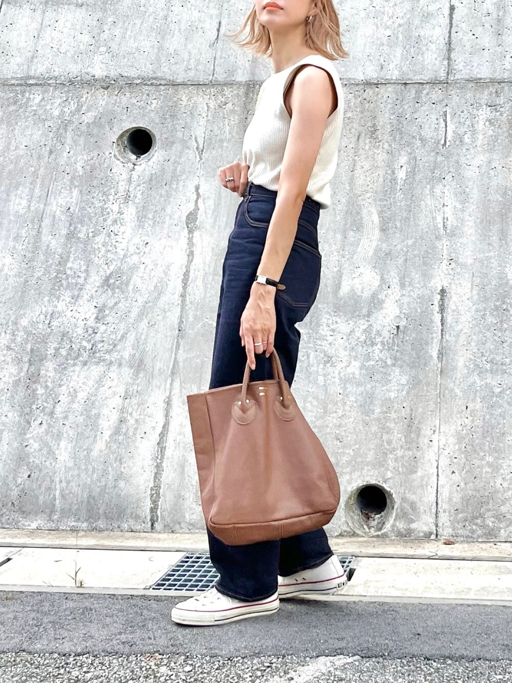 ホワイト系のニット/セーター、ブラウン系のトートバッグ、ブルー系のデニムパンツを着用したレディースの夏コーディネートの2枚目の写真
