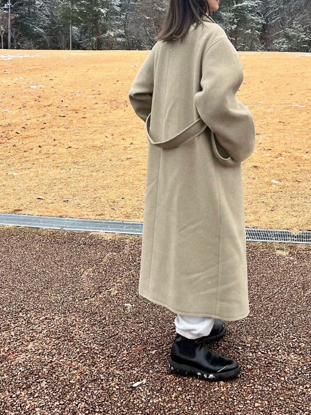 グリーン系のステンカラーコート、ホワイト系のスウェットパンツ、ブラック系のブーツを着用したレディースの冬コーディネートの2枚目の写真