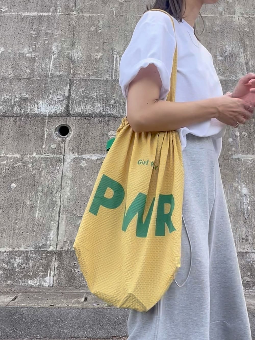 イエロー系のトートバッグ、グレー系のパンツ、ブラック系のスニーカーを着用したレディースの夏コーディネートの2枚目の写真