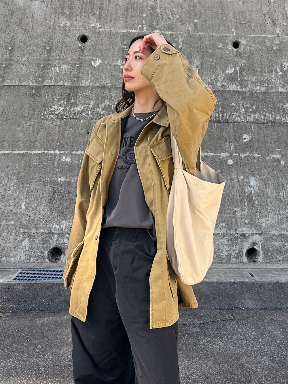 イエロー系のミリタリージャケット、ブラック系のショルダーバッグ、ホワイト系のデニムパンツを着用したレディースの春コーディネートの4枚目の写真