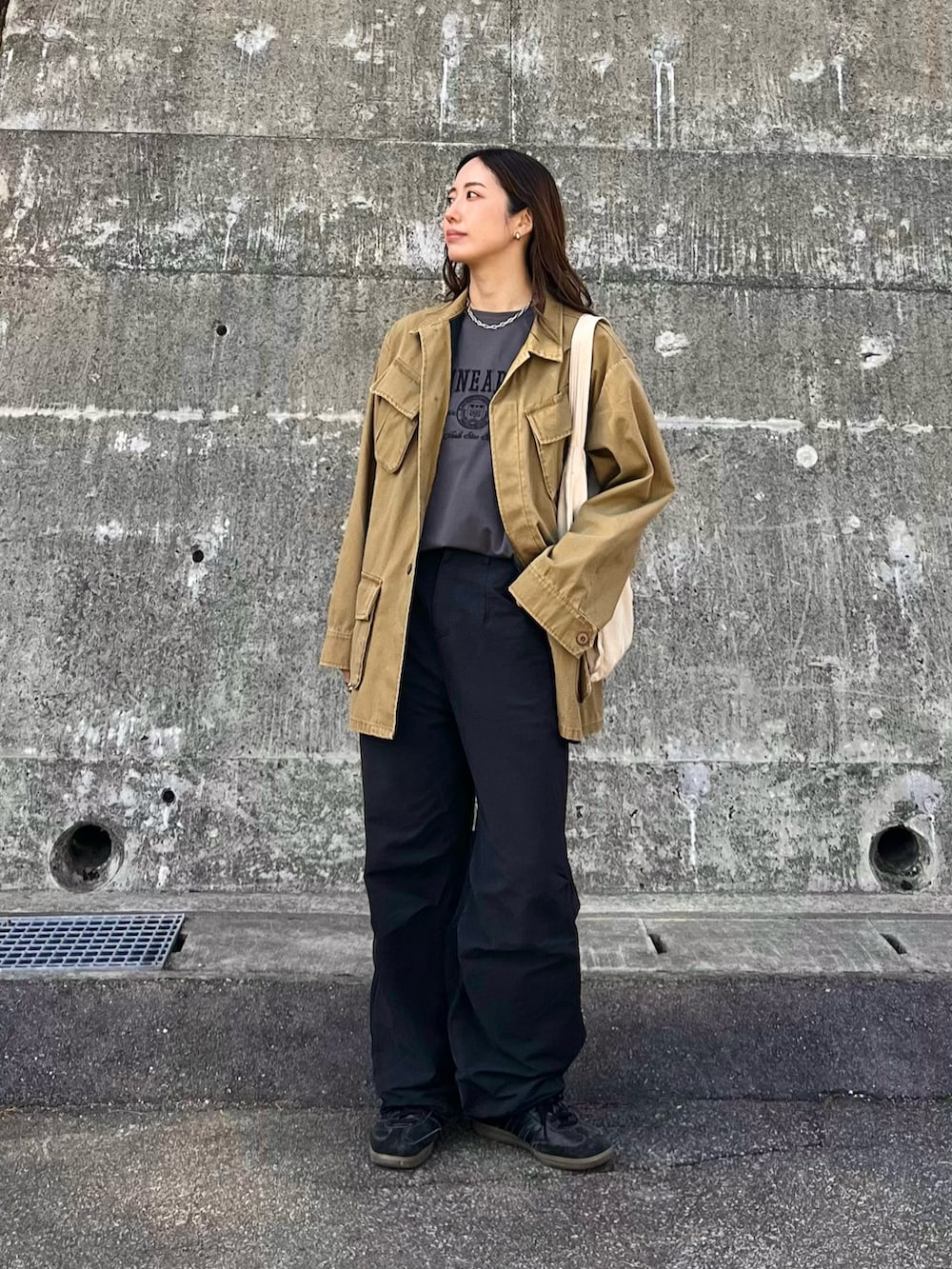 イエロー系のミリタリージャケット、ブラック系のショルダーバッグ、ホワイト系のデニムパンツを着用したレディースの春コーディネートの3枚目の写真