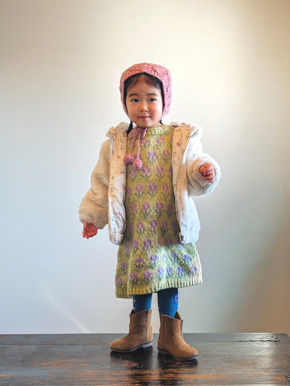 ベージュ系のブルゾン、グリーン系のワンピース、ブラウン系のブーツを着用したキッズの冬コーディネートの2枚目の写真