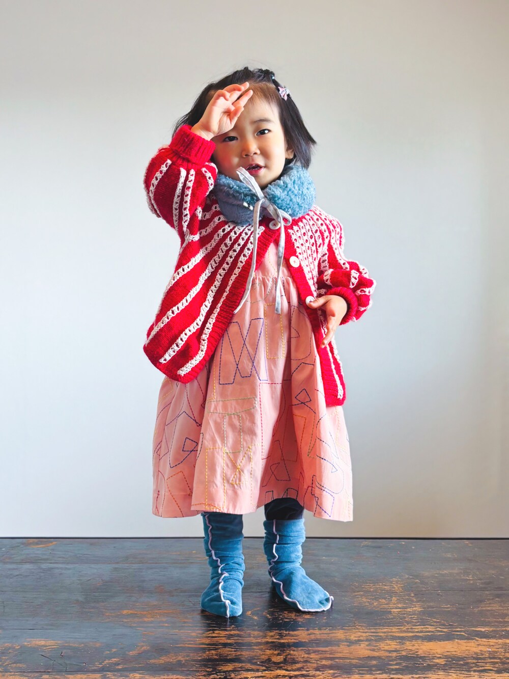 レッド系のニット/セーター、ブルー系のデニムパンツ、オレンジ系のワンピースを着用したキッズの冬コーディネートの2枚目の写真