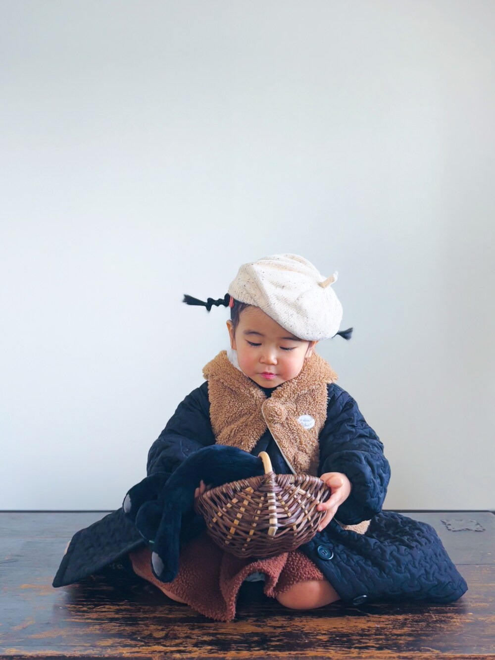 ブラウン系のかごバッグ、ブラック系のノーカラーコート、ブラウン系のベストを着用したキッズの冬コーディネートの3枚目の写真