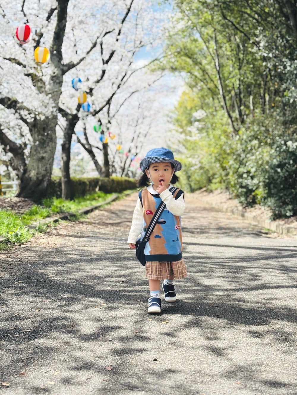 ブルー系のショルダーバッグ、その他のベスト、ベージュ系のワンピースを着用したキッズの春コーディネートの2枚目の写真