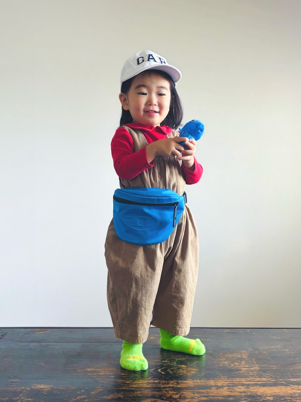 ブルー系のボディバッグ/ウエストポーチ、ベージュ系のつなぎ/オールインワン、ホワイト系のキャップを着用したキッズの春コーディネートの3枚目の写真