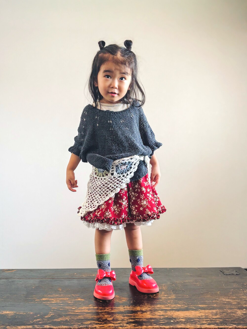 ブラック系のニット/セーター、ベージュ系のTシャツ/カットソー、レッド系のスカートを着用したキッズの秋コーディネートの2枚目の写真