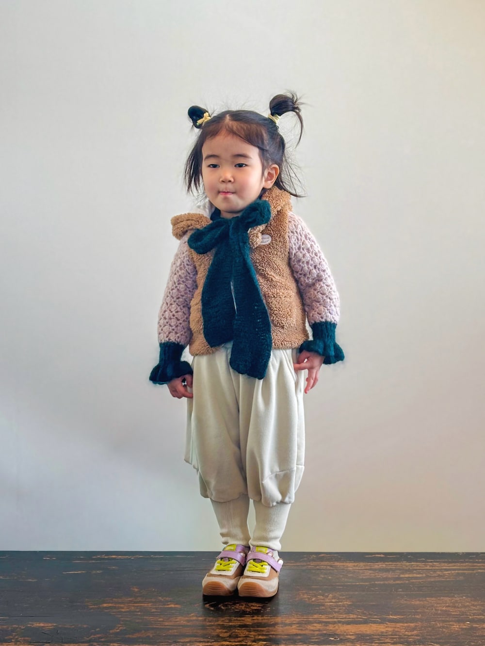 イエロー系のスニーカー、ピンク系のニット/セーター、ブラウン系のベストを着用したキッズの冬コーディネートの2枚目の写真