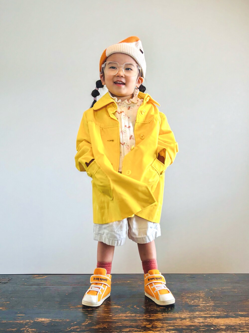 オレンジ系のスニーカー、ベージュ系のシャツ/ブラウス、イエロー系のステンカラーコートを着用したキッズの秋コーディネートの2枚目の写真