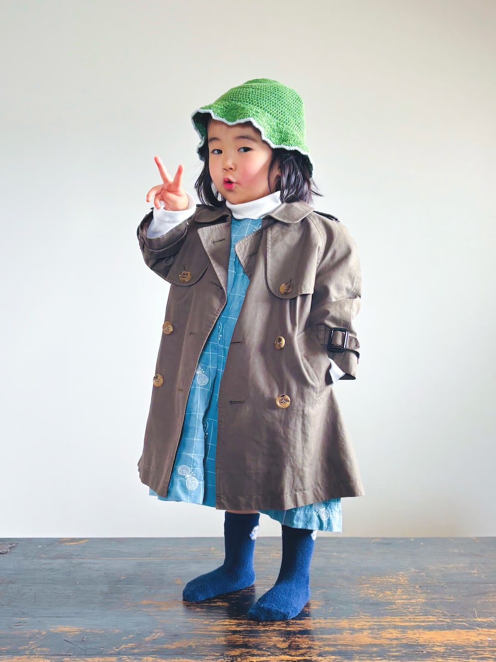 グリーン系のトレンチコート、ホワイト系のTシャツ/カットソー、ブルー系のワンピースを着用したキッズの春コーディネートの2枚目の写真