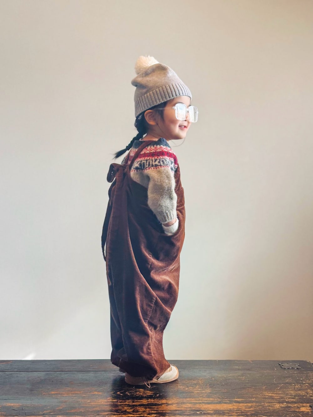 イエロー系のスニーカー、ベージュ系のニット/セーター、ブラウン系のサロペット/オーバーオールを着用したキッズの冬コーディネートの2枚目の写真