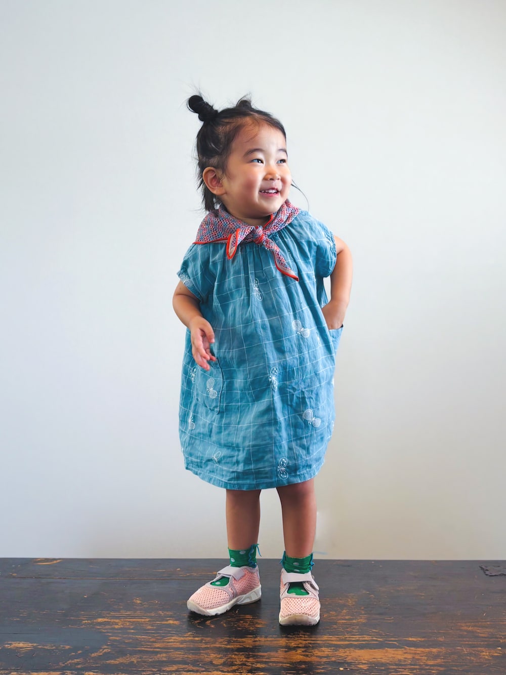 ピンク系のスニーカー、ブルー系のワンピース、オレンジ系のバンダナ/スカーフを着用したキッズの夏コーディネートの2枚目の写真