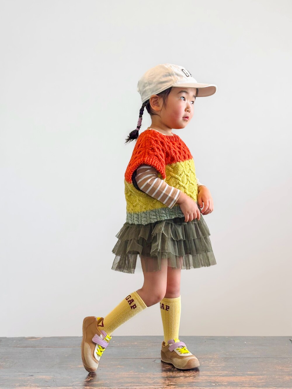 グリーン系のスカート、イエロー系のスニーカー、その他のベストを着用したキッズの春コーディネートの2枚目の写真