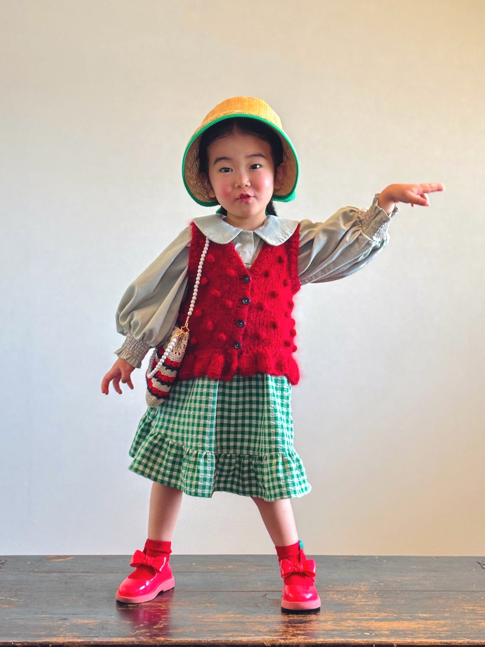 グリーン系のスカート、レッド系のベスト、グリーン系のシャツ/ブラウスを着用したキッズの春コーディネートの3枚目の写真