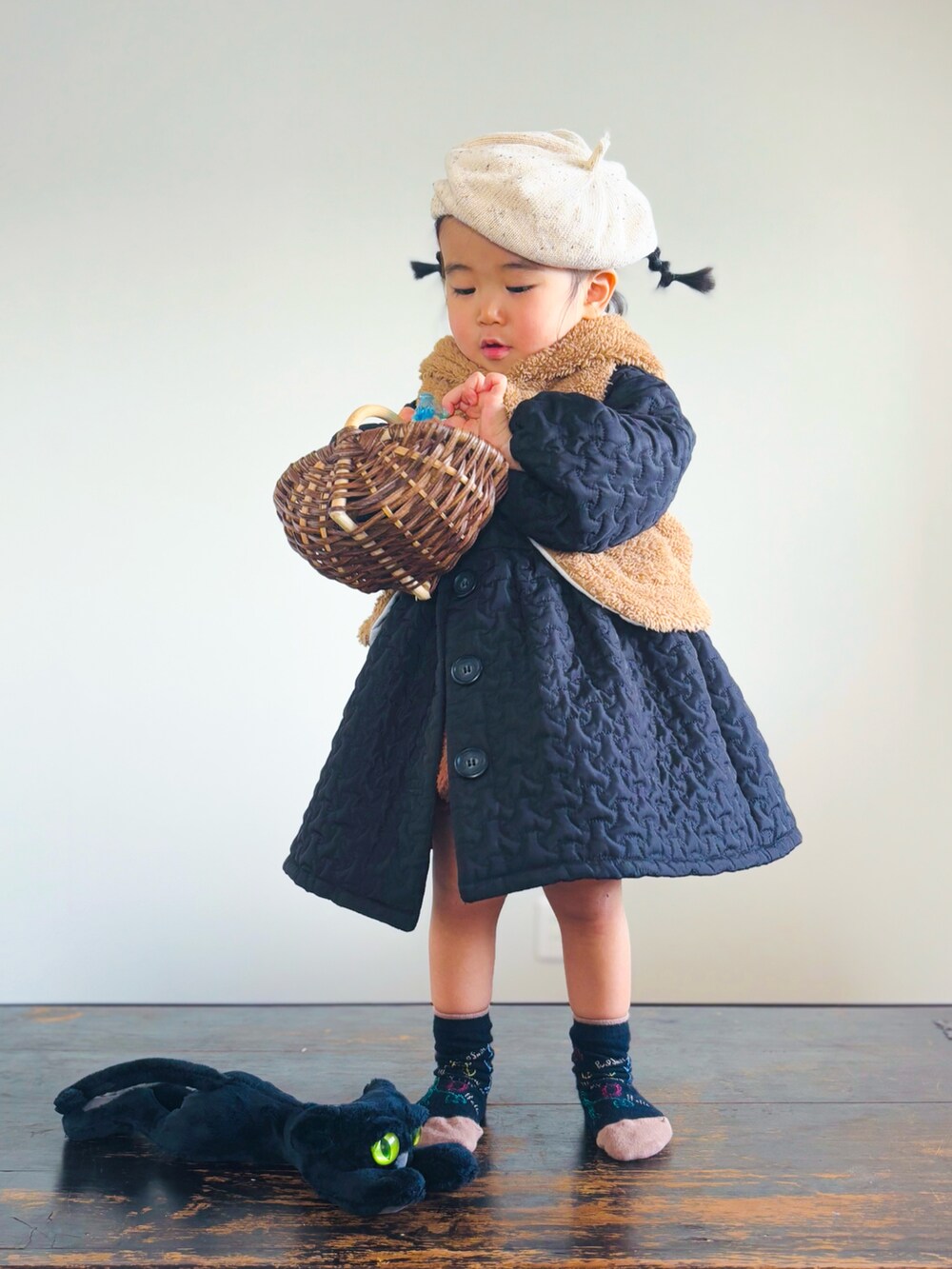 ブラウン系のかごバッグ、ブラック系のノーカラーコート、ブラウン系のベストを着用したキッズの冬コーディネートの2枚目の写真