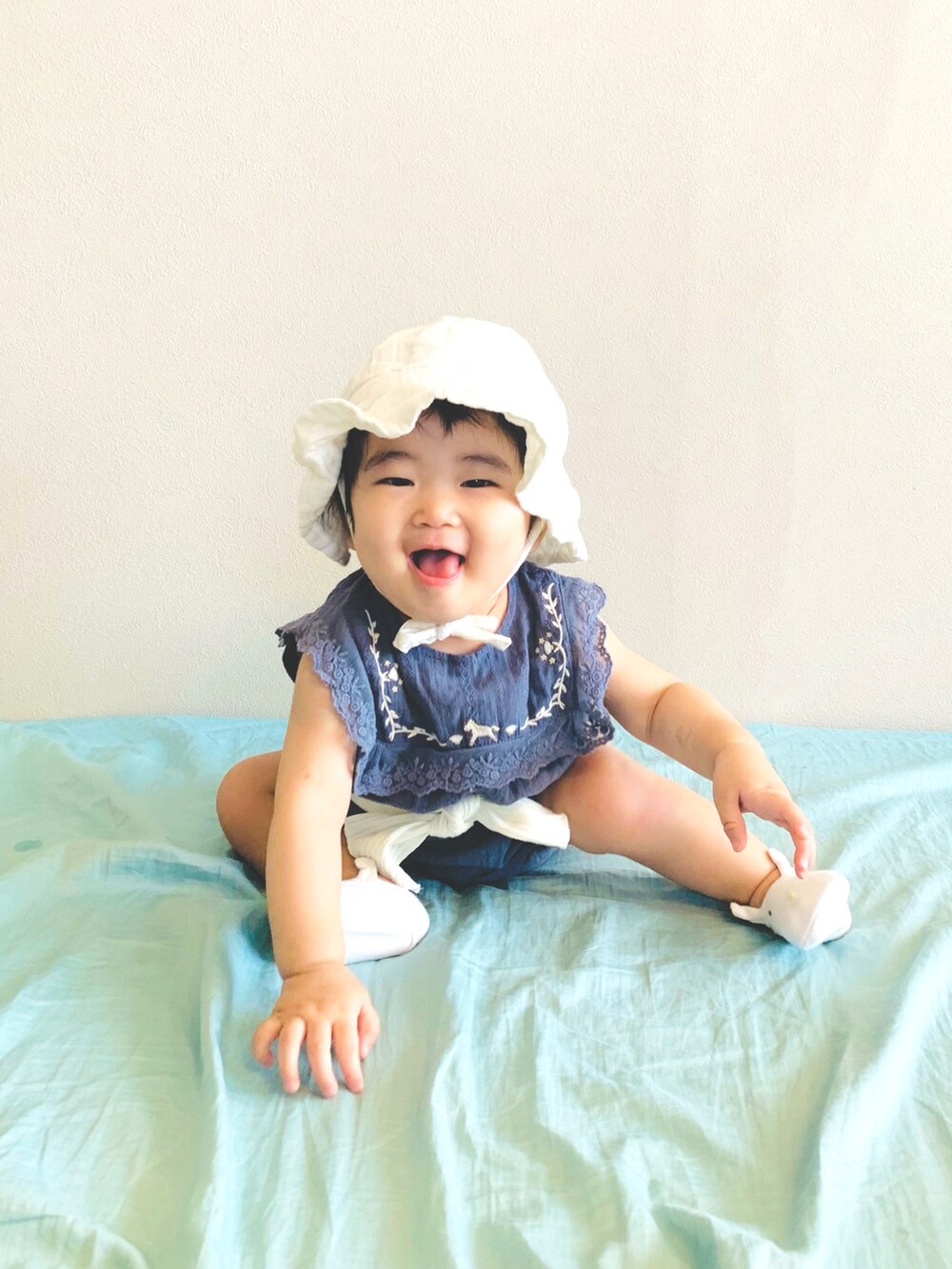 ホワイト系のハット、ブルー系のロンパース、ホワイト系のヘアバンドを着用したキッズの夏コーディネートの2枚目の写真
