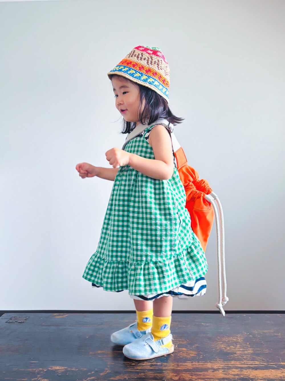 グリーン系のスカート、ブラック系のワンピース、オレンジ系のショルダーバッグを着用したキッズの夏コーディネートの4枚目の写真
