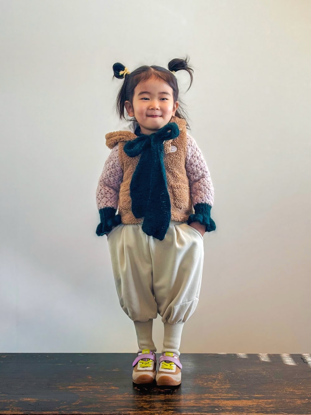 イエロー系のスニーカー、ピンク系のニット/セーター、ブラウン系のベストを着用したキッズの冬コーディネートの3枚目の写真