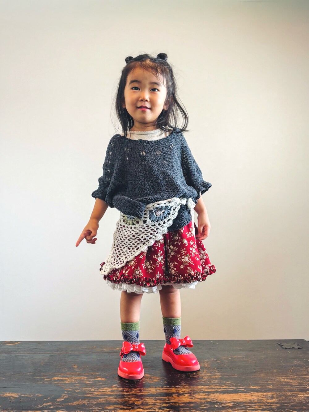 ブラック系のニット/セーター、ベージュ系のTシャツ/カットソー、レッド系のスカートを着用したキッズの秋コーディネートの3枚目の写真