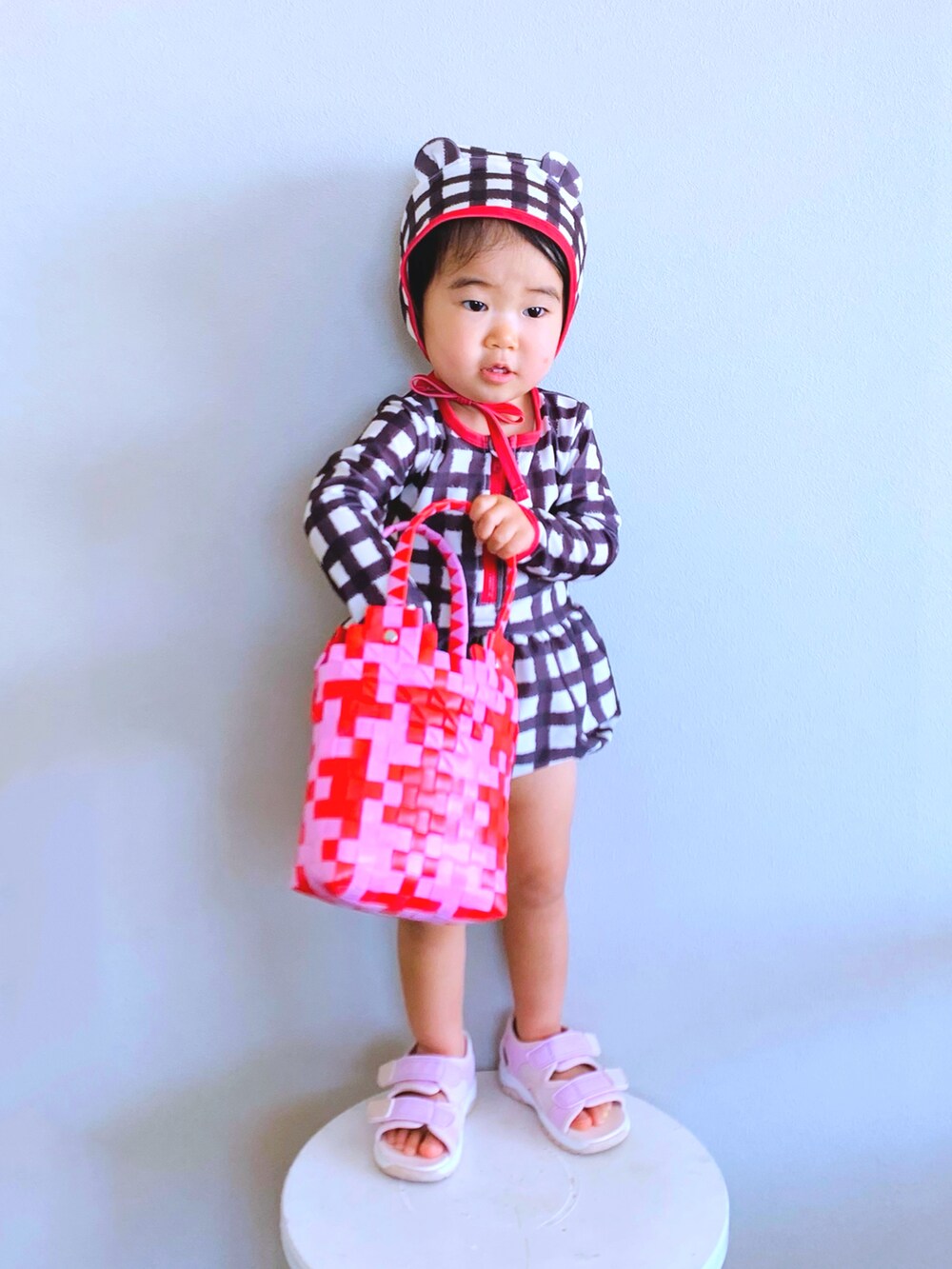 ピンク系のサンダル、ピンク系のかごバッグ、ブラック系のラッシュガードを着用したキッズの夏コーディネートの2枚目の写真