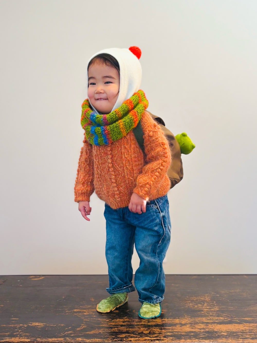 ブルー系のデニムパンツ、オレンジ系のニット/セーター、グリーン系のバックパック/リュックを着用したキッズの冬コーディネートの2枚目の写真