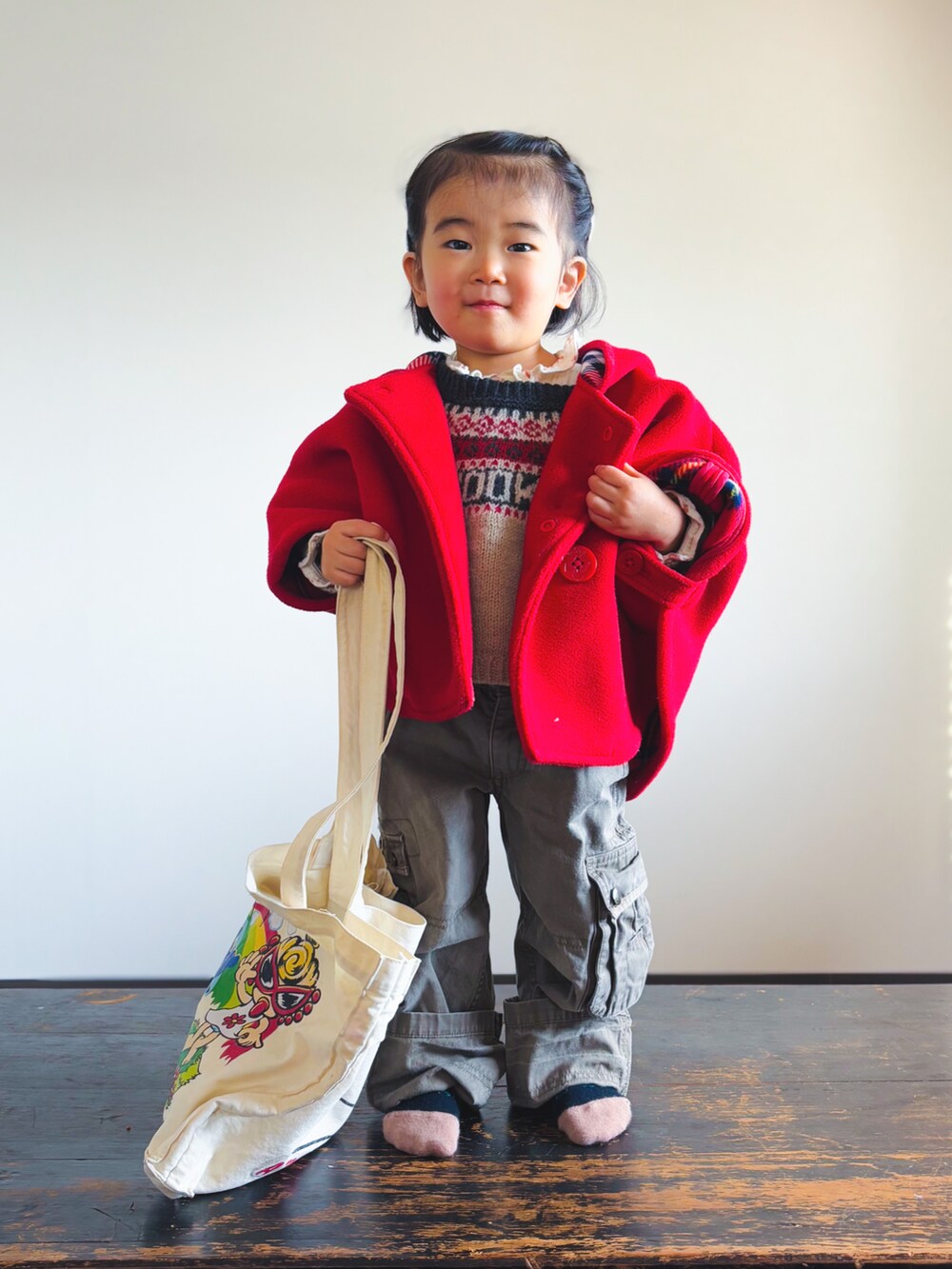 レッド系のポンチョ、ベージュ系のニット/セーター、ベージュ系のシャツ/ブラウスを着用したキッズの冬コーディネートの2枚目の写真