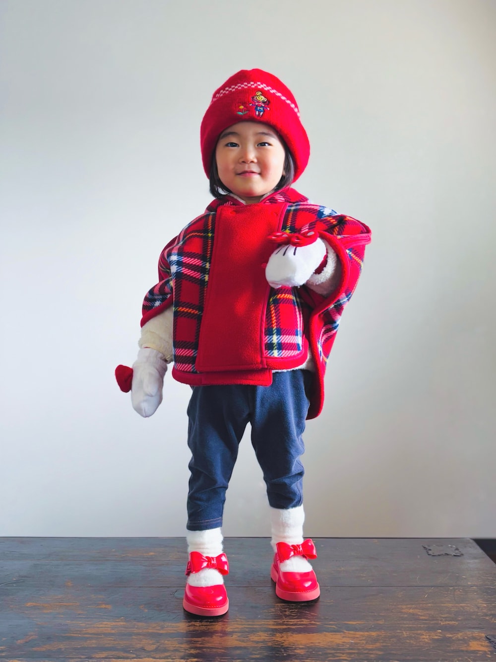 ブルー系のデニムパンツ、レッド系のドレスシューズ、レッド系のポンチョを着用したキッズの冬コーディネートの2枚目の写真