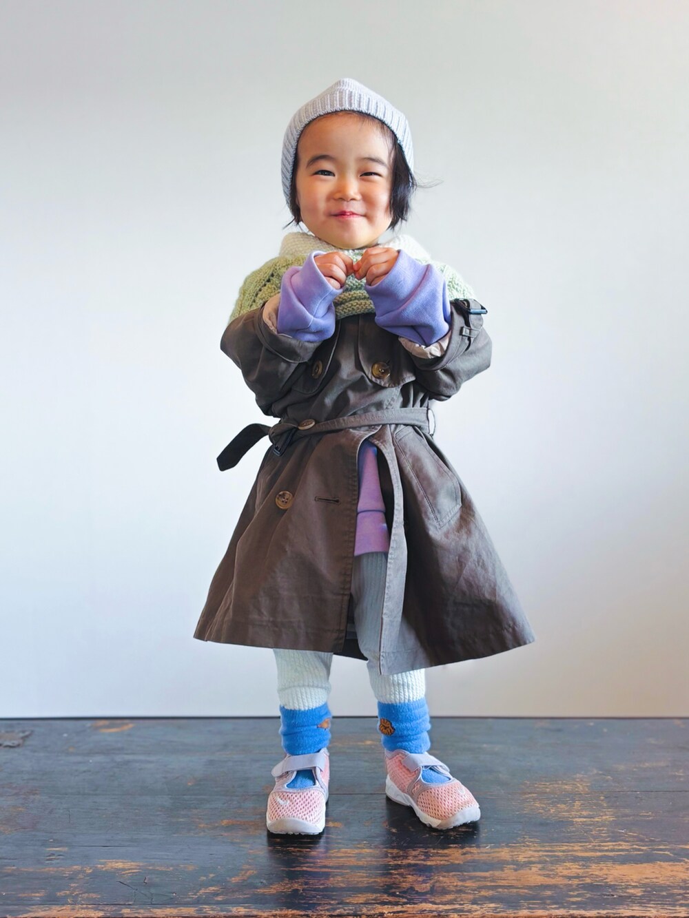 グリーン系のポンチョ、グリーン系のトレンチコート、パープル系のスウェットを着用したキッズの冬コーディネートの2枚目の写真