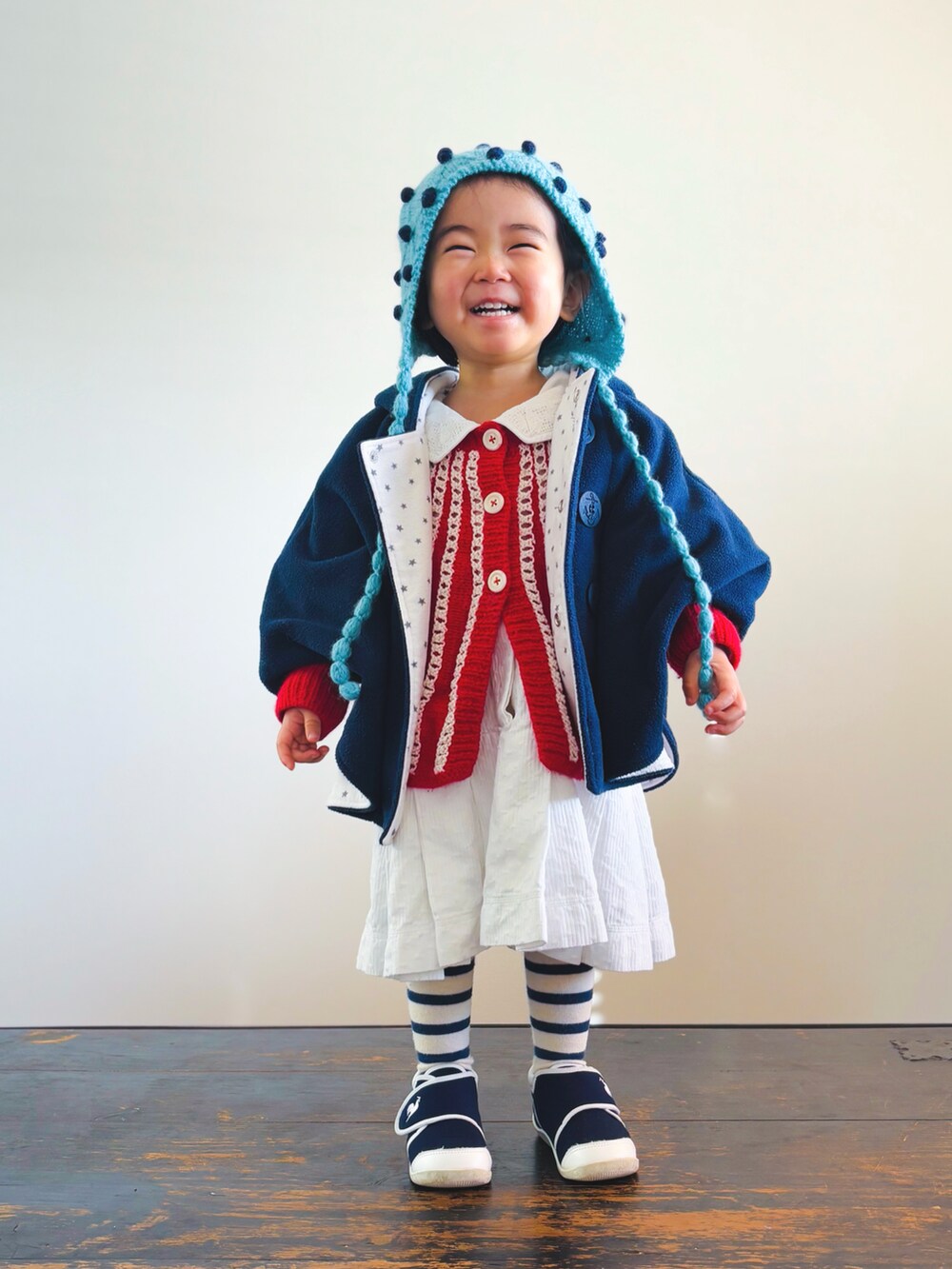 ブルー系のスニーカー、ホワイト系のワンピース、ブラック系のポンチョを着用したキッズの冬コーディネートの3枚目の写真