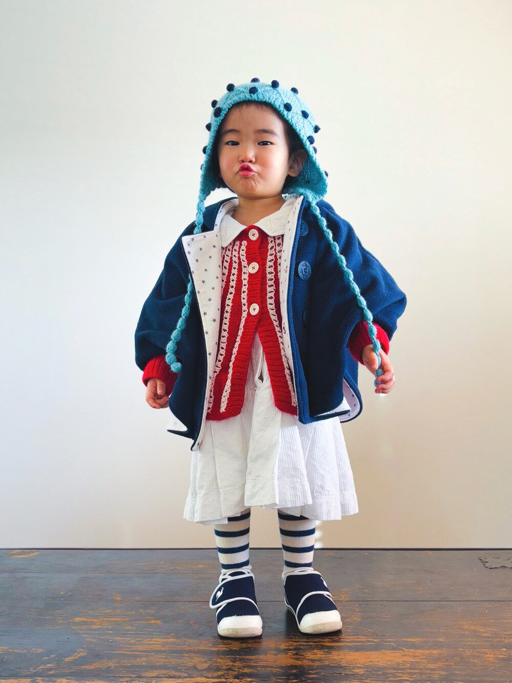 ブルー系のスニーカー、ホワイト系のワンピース、ブラック系のポンチョを着用したキッズの冬コーディネートの2枚目の写真