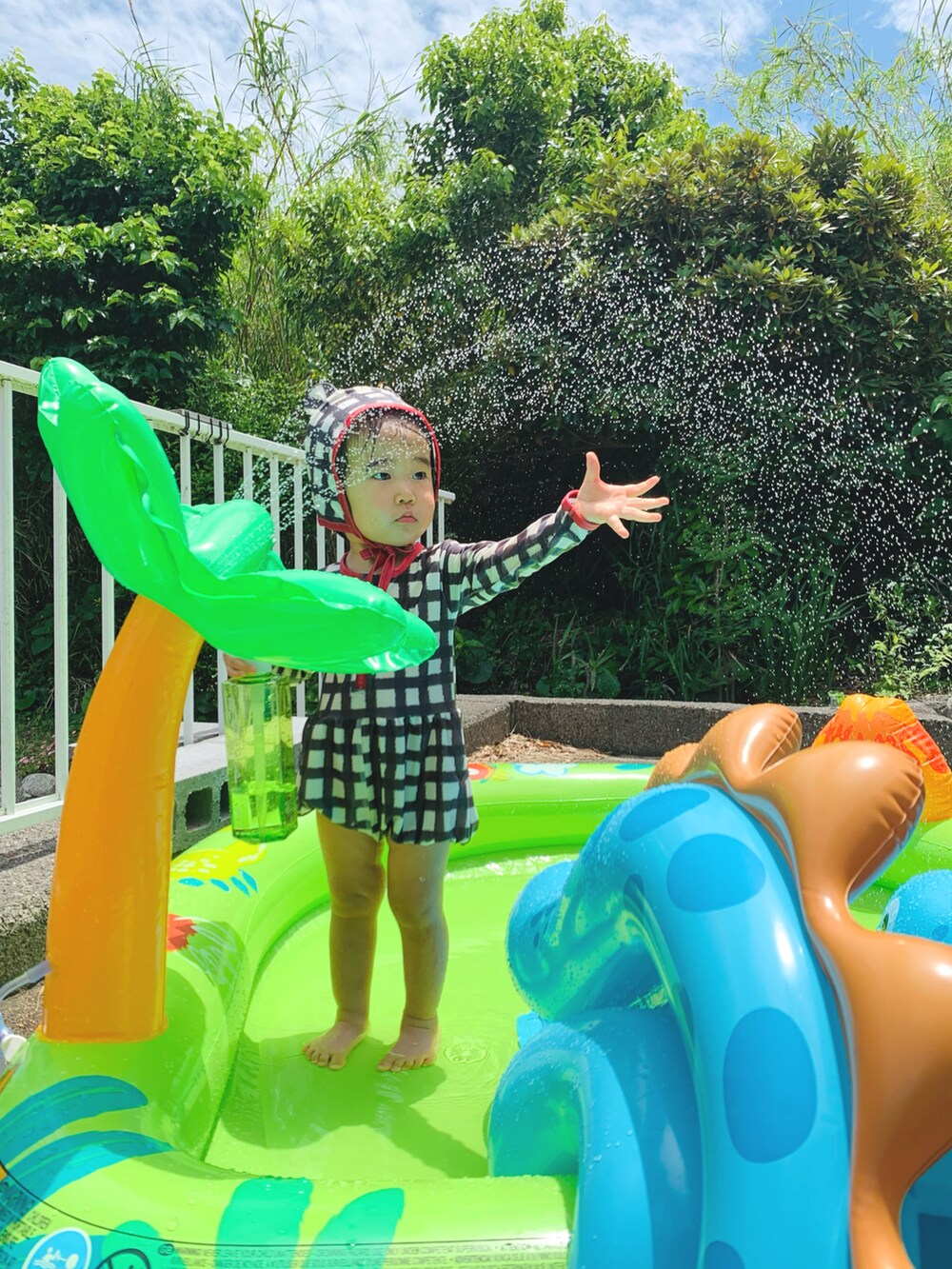 ピンク系のサンダル、ピンク系のかごバッグ、ブラック系のラッシュガードを着用したキッズの夏コーディネートの3枚目の写真