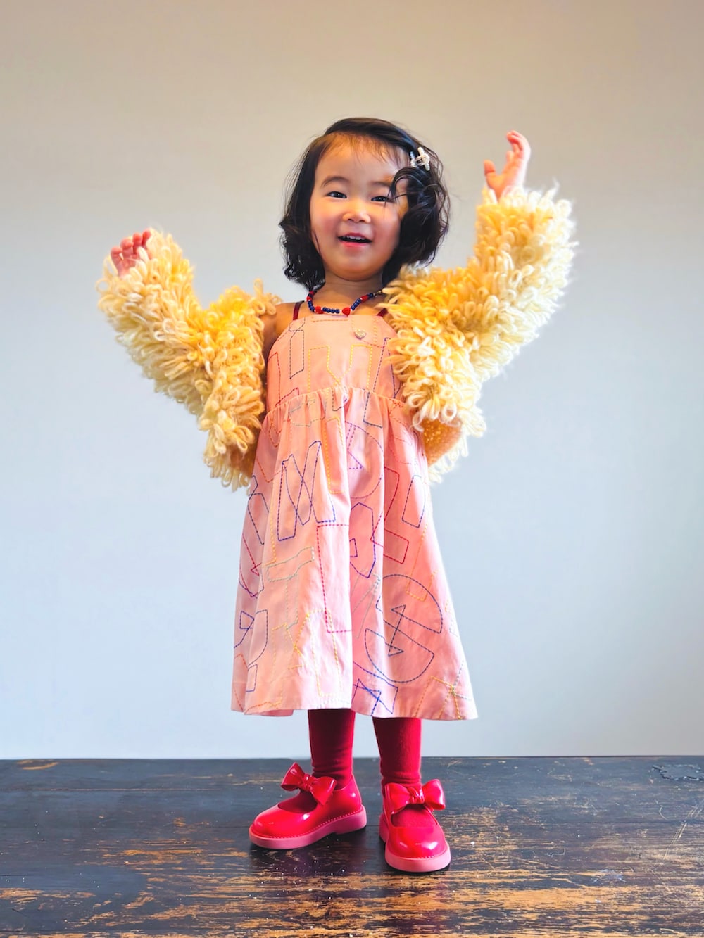 レッド系のドレスシューズ、オレンジ系のワンピース、イエロー系のジャケット/アウターを着用したキッズの春コーディネートの2枚目の写真