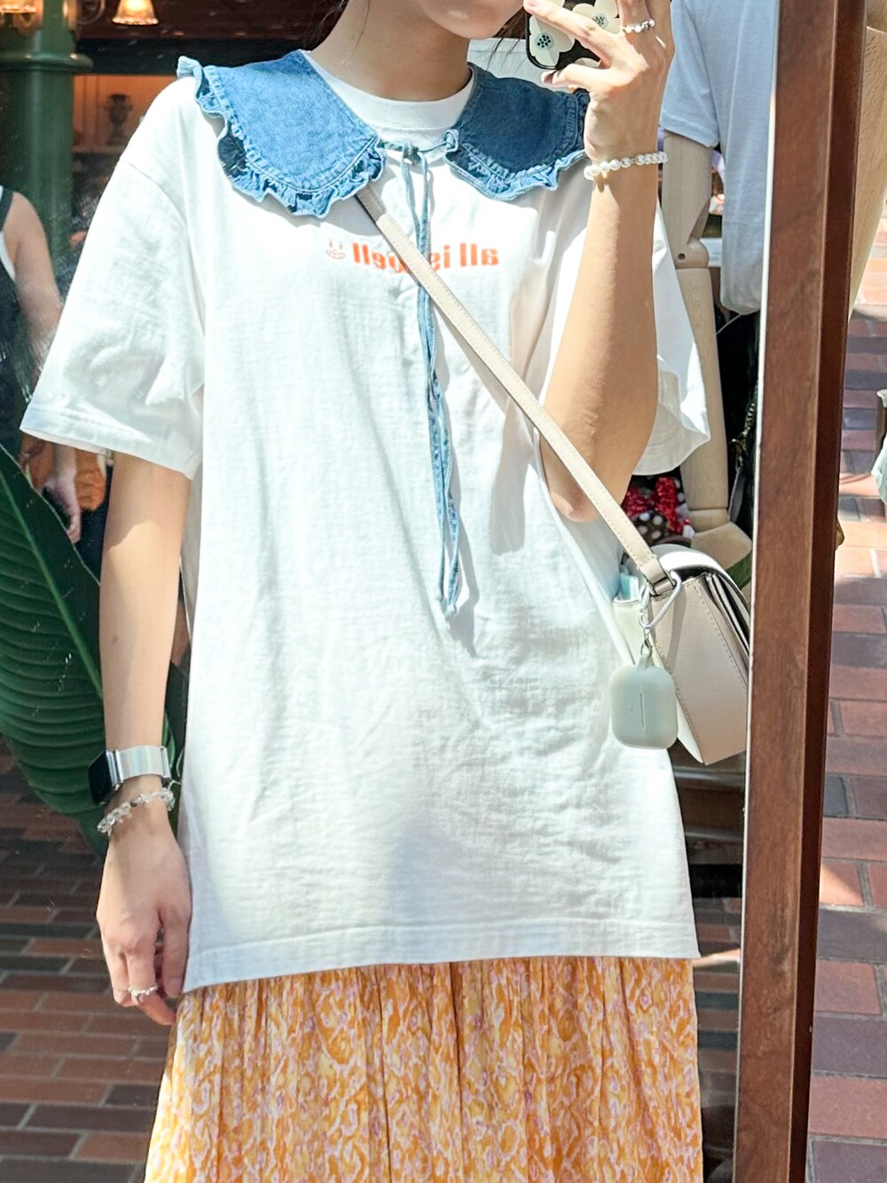 オレンジ系のスカート、ホワイト系のバッグ、ブルー系のスニーカーを着用したレディースの夏コーディネートの3枚目の写真