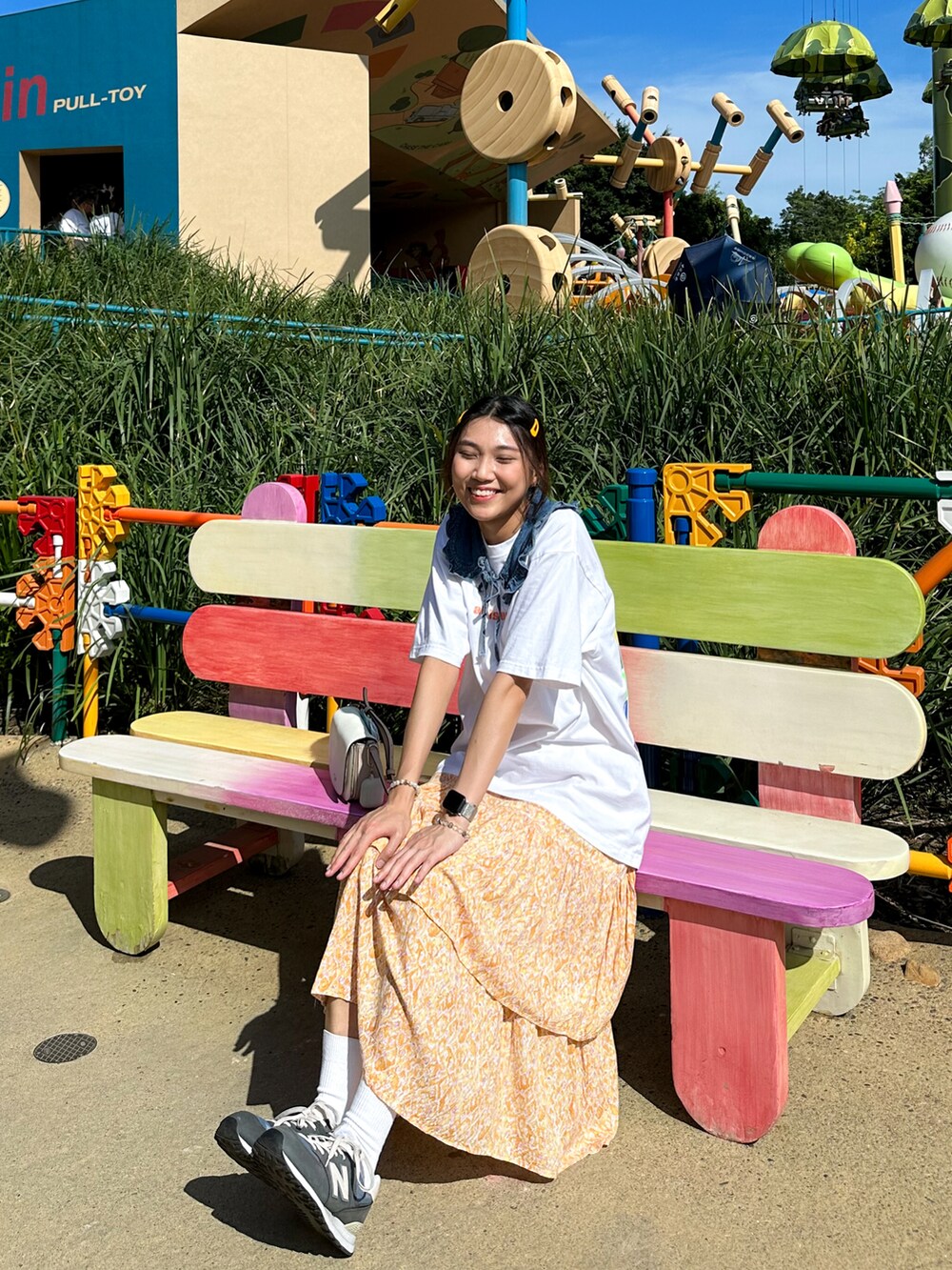 オレンジ系のスカート、ホワイト系のバッグ、ブルー系のスニーカーを着用したレディースの夏コーディネートの2枚目の写真