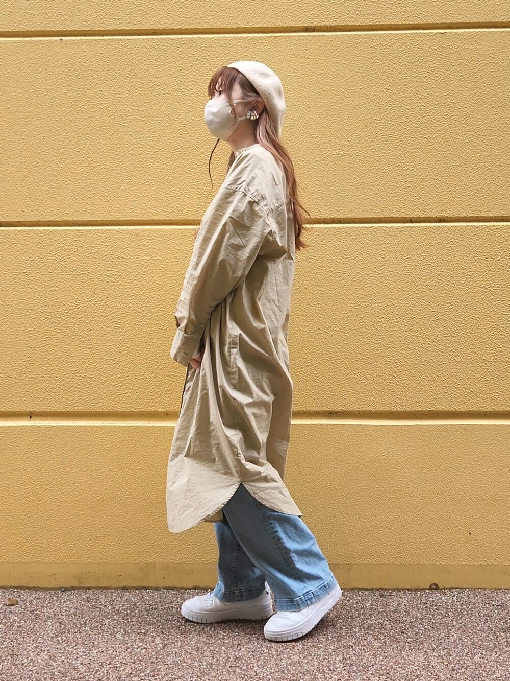 ベージュ系のワンピース、ブルー系のデニムパンツ、ホワイト系のスニーカーを着用したレディースの春コーディネートの2枚目の写真